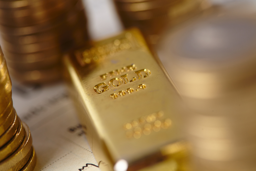 Goldbarren neben Geldmünzen und Aktiengraph
